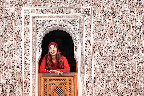 Young woman wearing a red turban looking out from a window of the Ben Youssef Medersa in Marrakech, Morocco